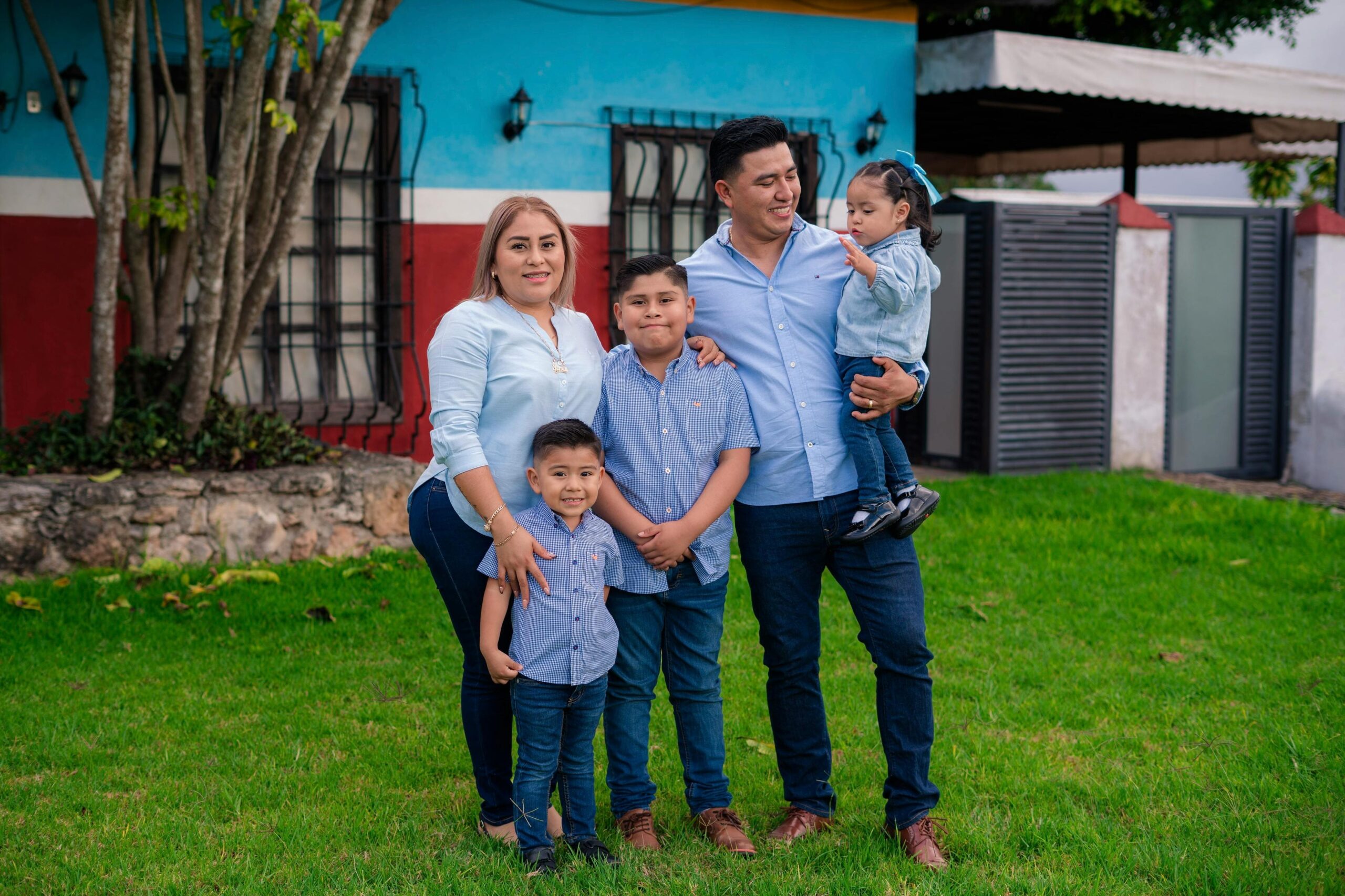 Candid family portrait outdoors with vibrant house background.