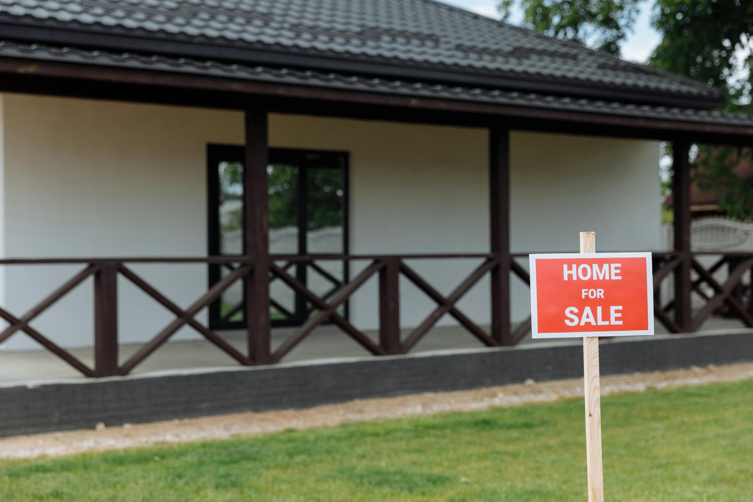 White house with porch and 'Home for Sale' sign on a sunny day.