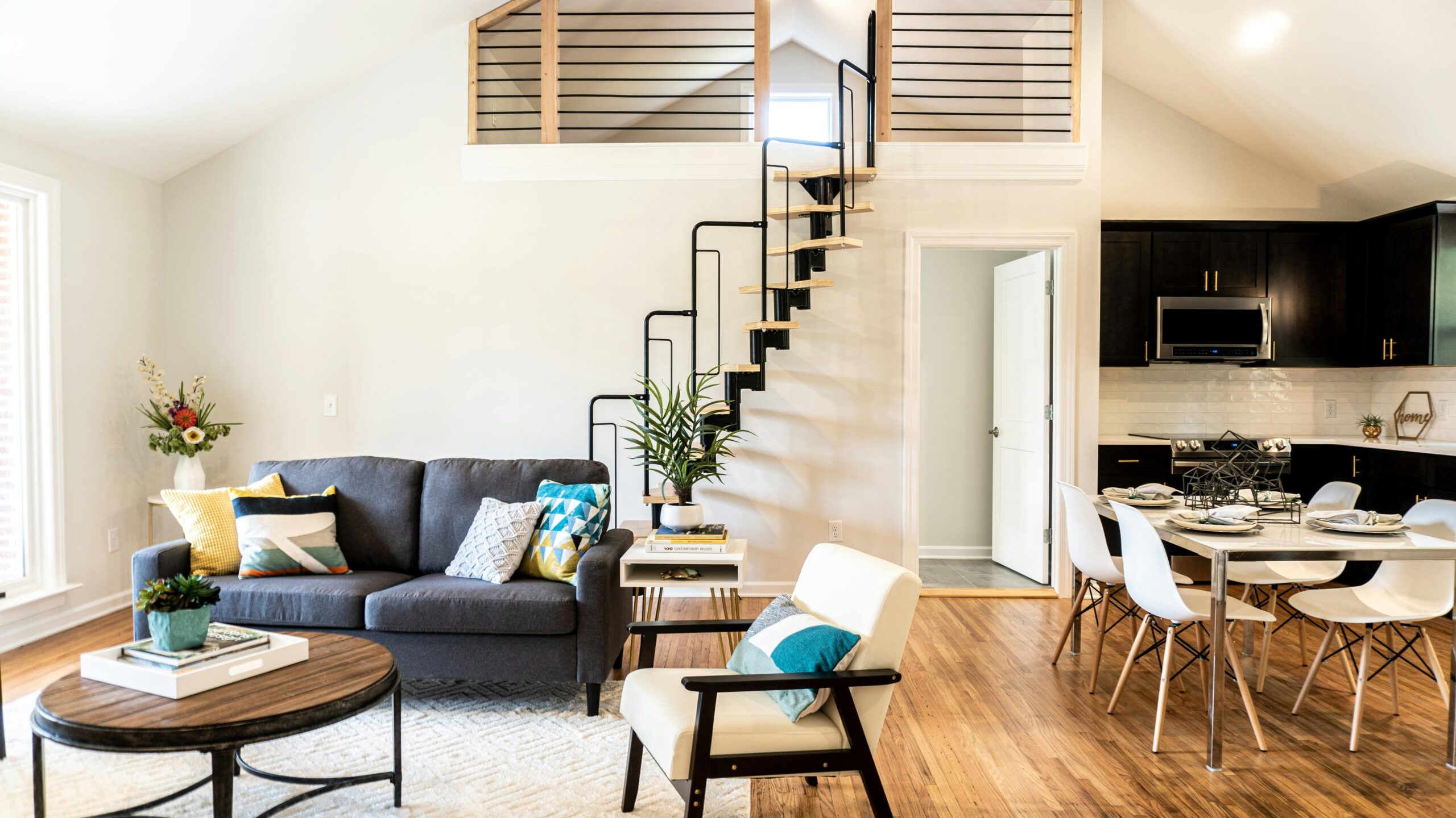 East Nashville cottage Stylish living space featuring a gray sofa, dining area, and spiral stairs in Nashville.