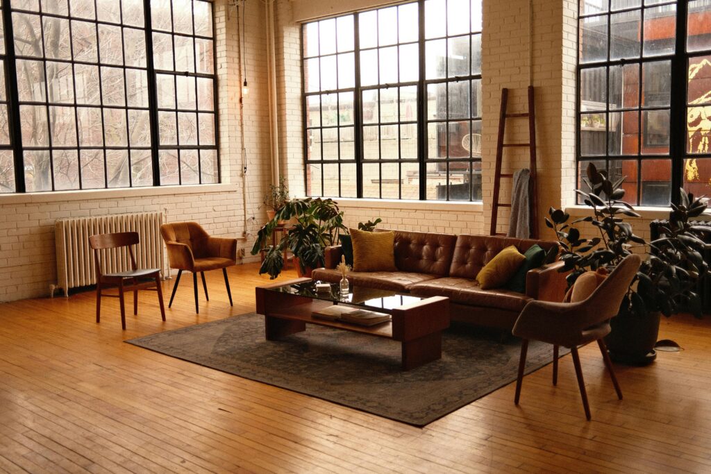 Spacious loft-style living room with modern furniture, large windows, and warm lighting.