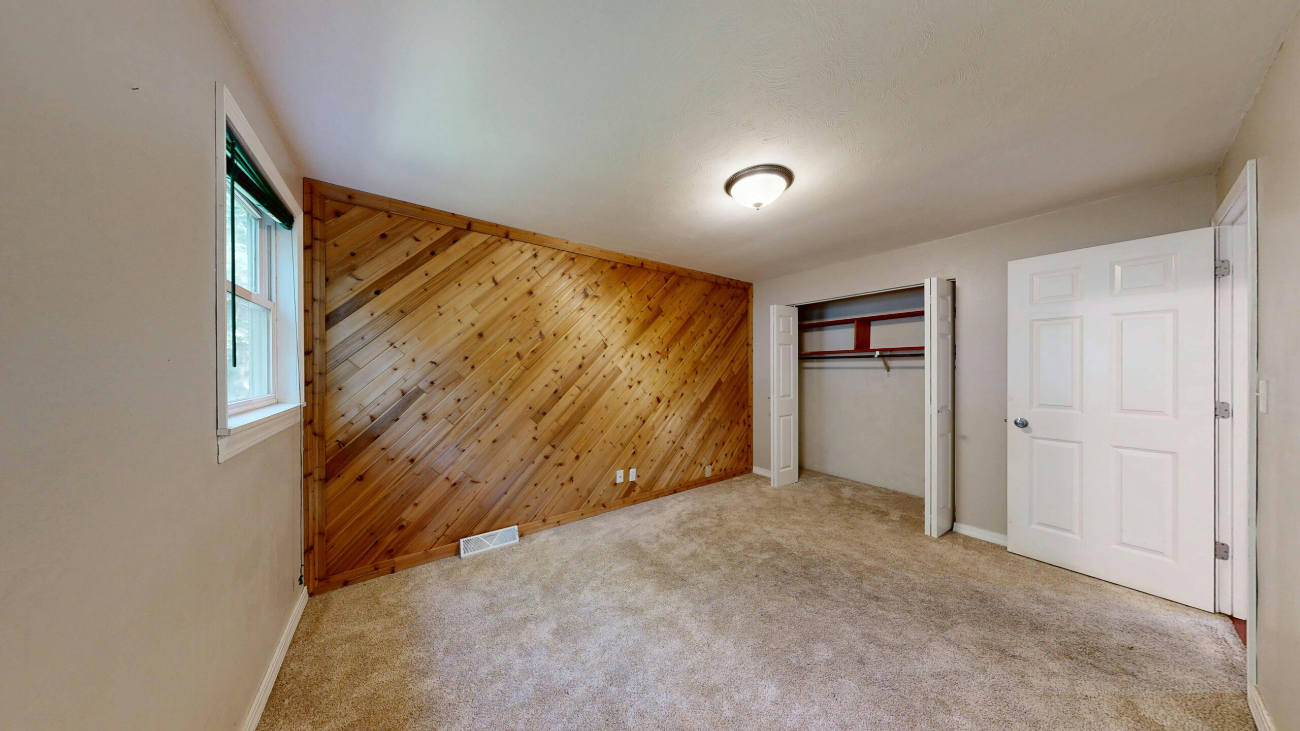Craftsman bungalow Spacious empty room featuring a wooden accent wall and carpet flooring.