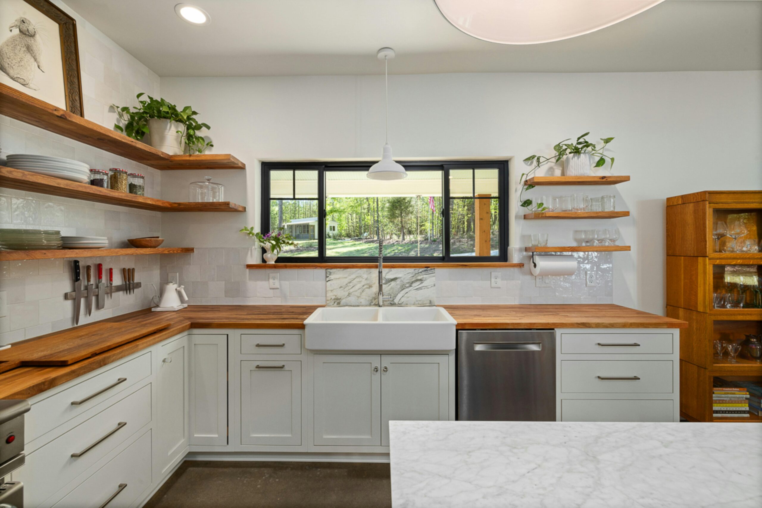 Tudor revival near City Park Stylish kitchen featuring open shelving, farmhouse sink, and wooden countertops with a view outside.