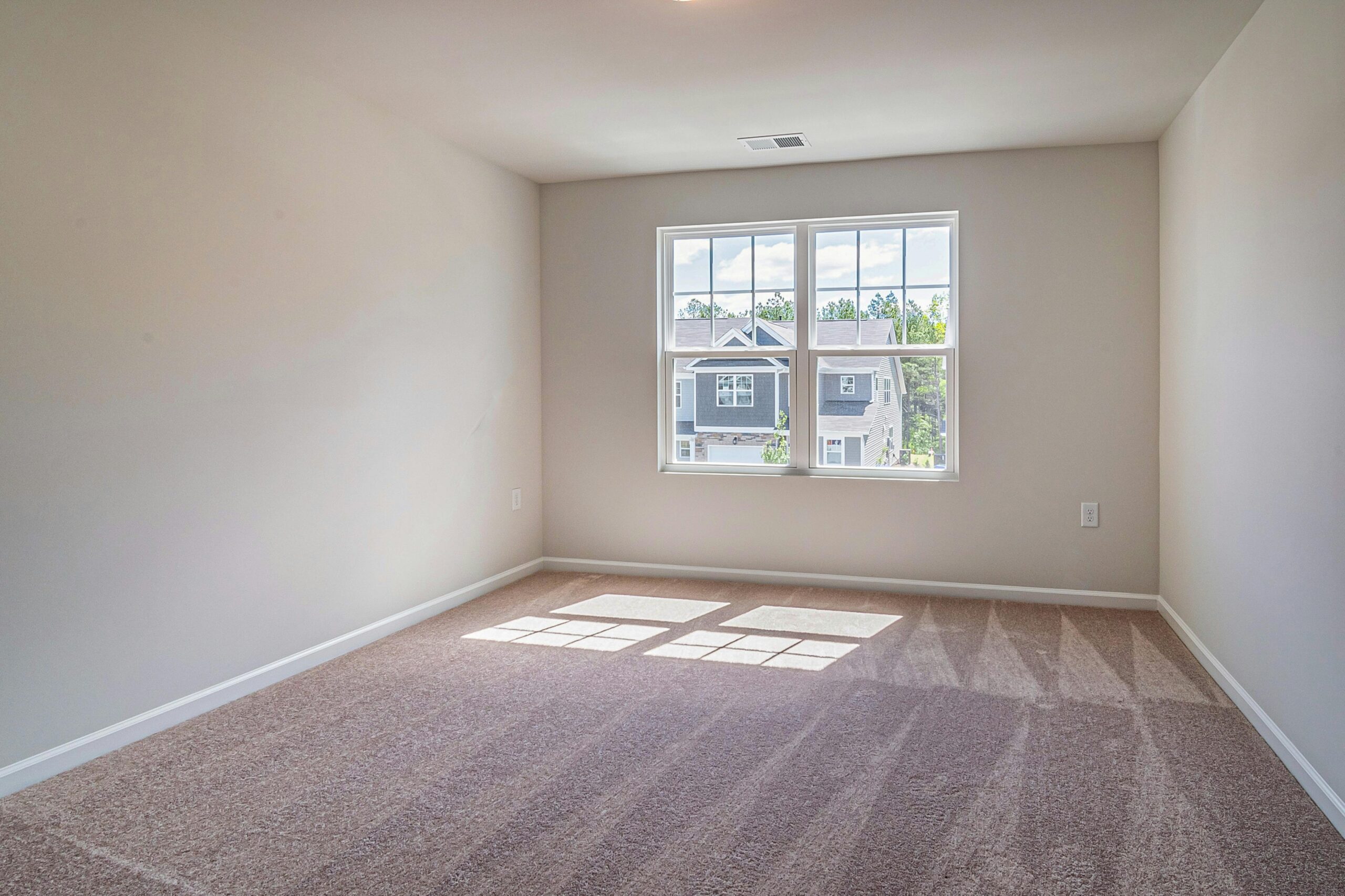 Sunlit empty room with carpet flooring, featuring a large window providing natural light.