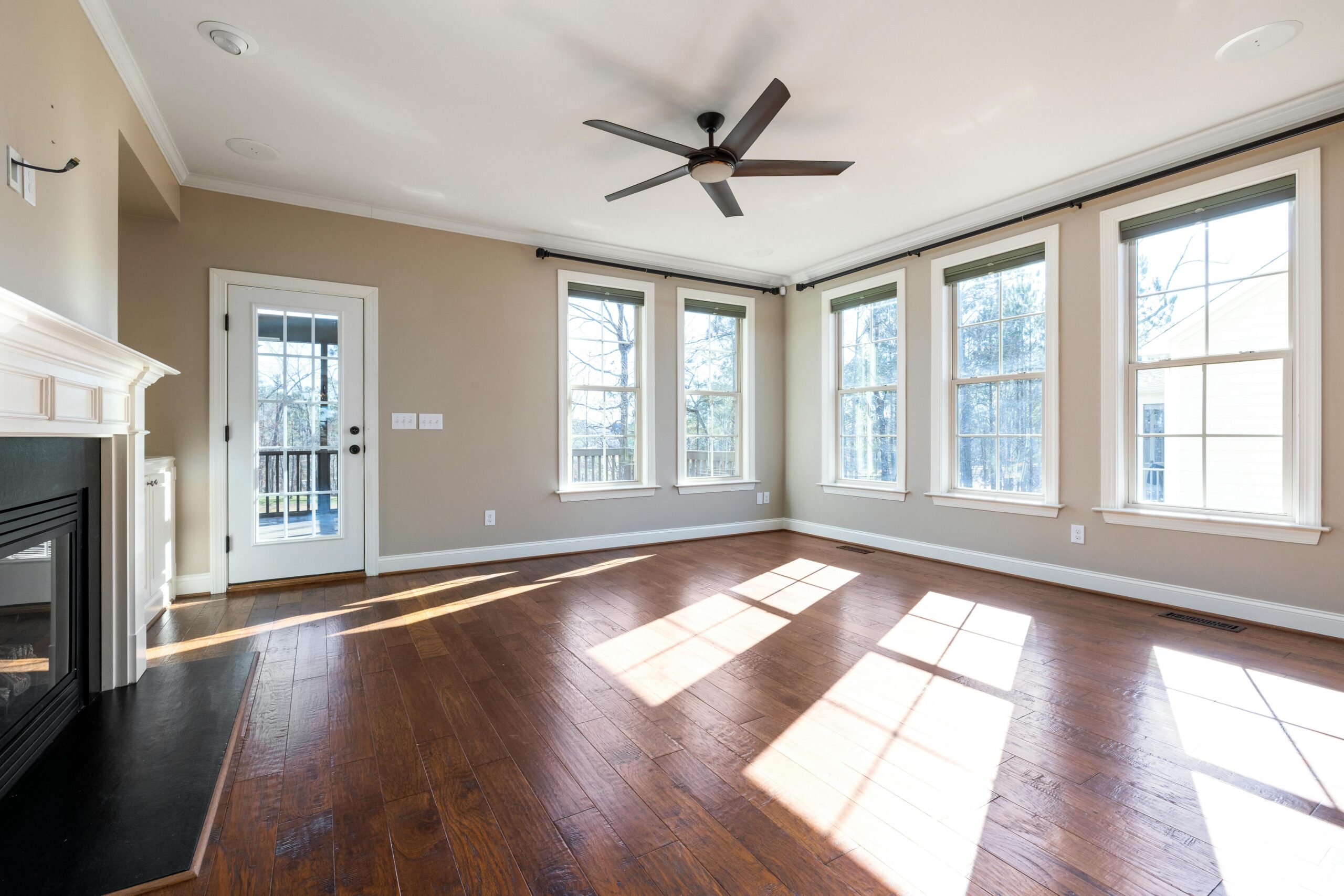 Craftsman bungalow Bright and empty living room with hardwood floor, ceiling fan, and large windows.